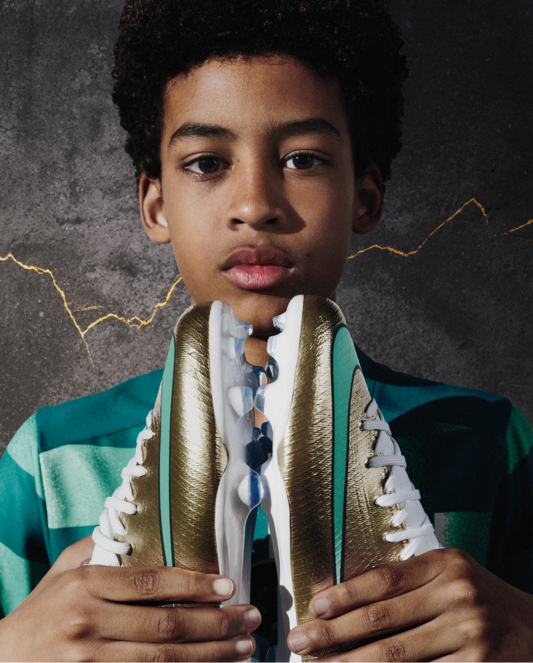 Portrait of a young boy holding both boots against his chest as he stares into the camera.