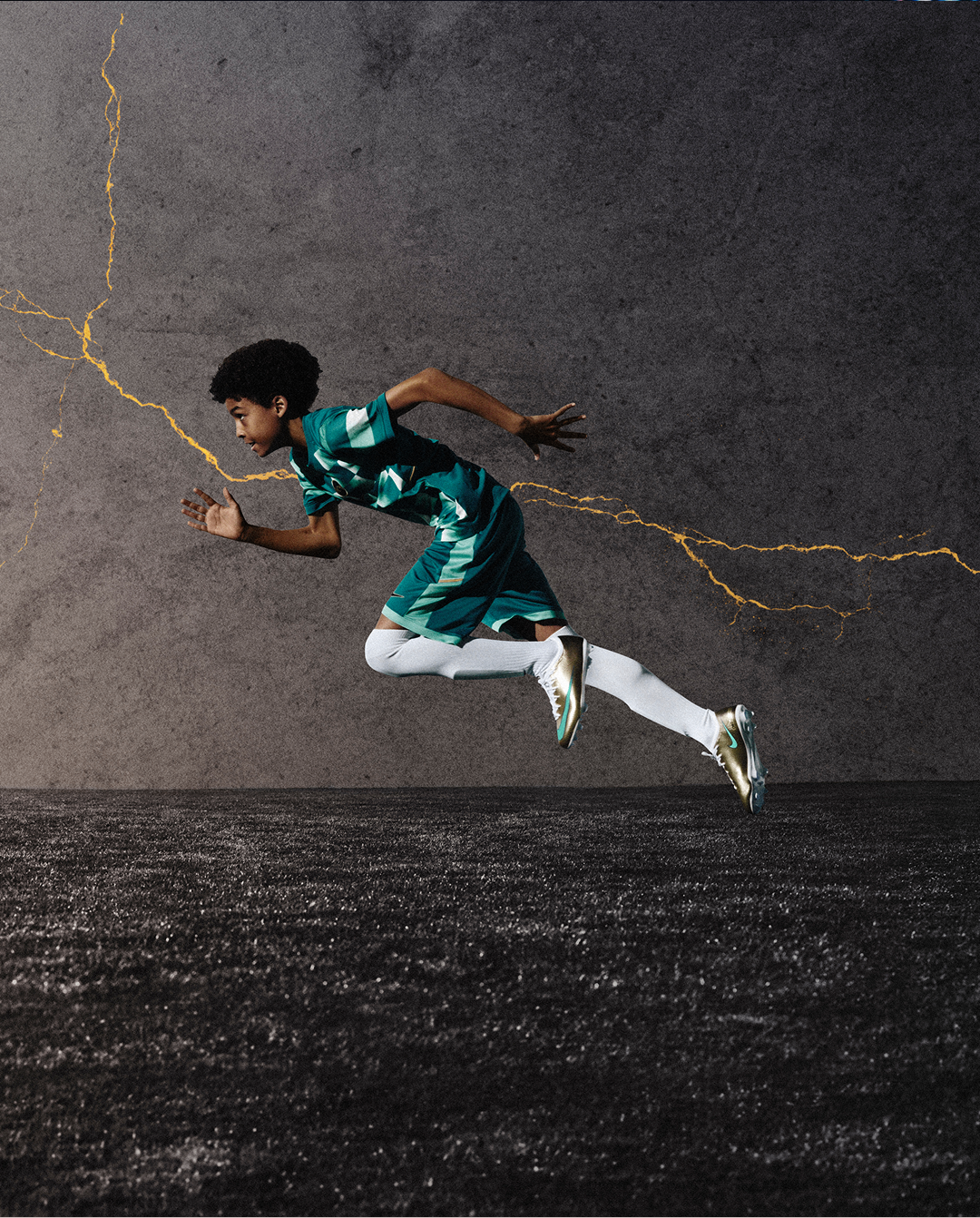 A young boy runs across a dark colored pitch with a crack of gold in the background.